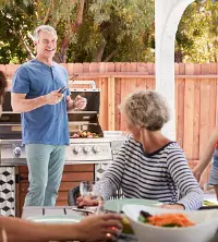 A man grilling outside and talking with others