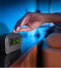 A man hitting snooze on his alarm clock